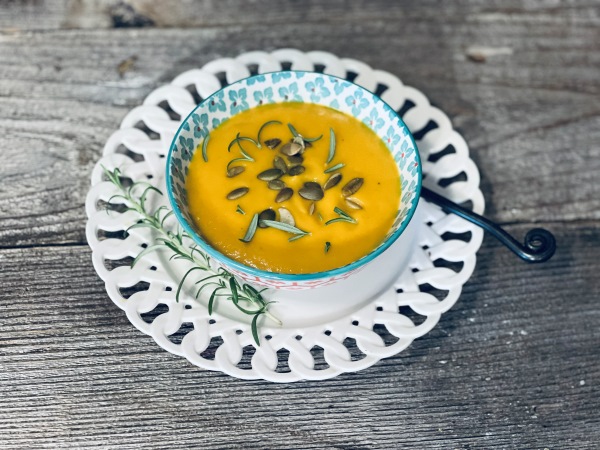 Butternut squash soup in a bowl garnished with pepitas, rosemary, sitting on a wooden table.