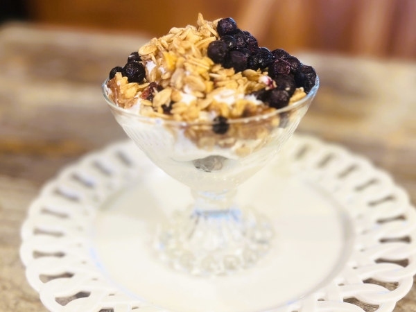 Yogurt in a glass cup topped with granola and blueberries.